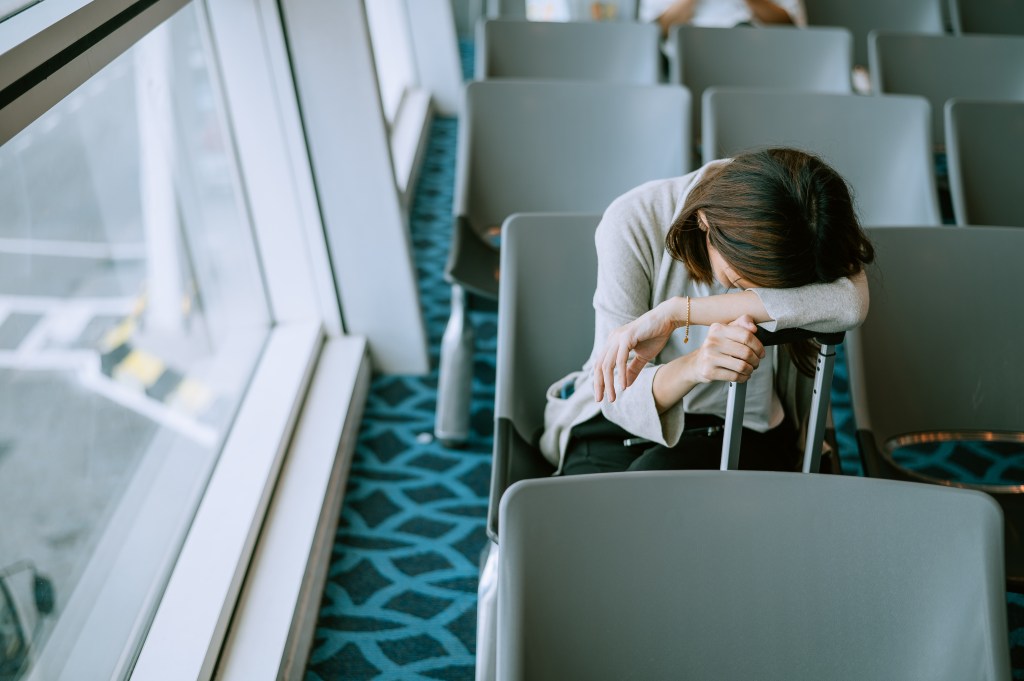 Young woman sleeping in a chair in an airport waiting area with a commercial airplane in the background