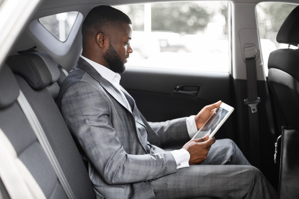 Concentrated black guy manager using digital tablet in luxury car.